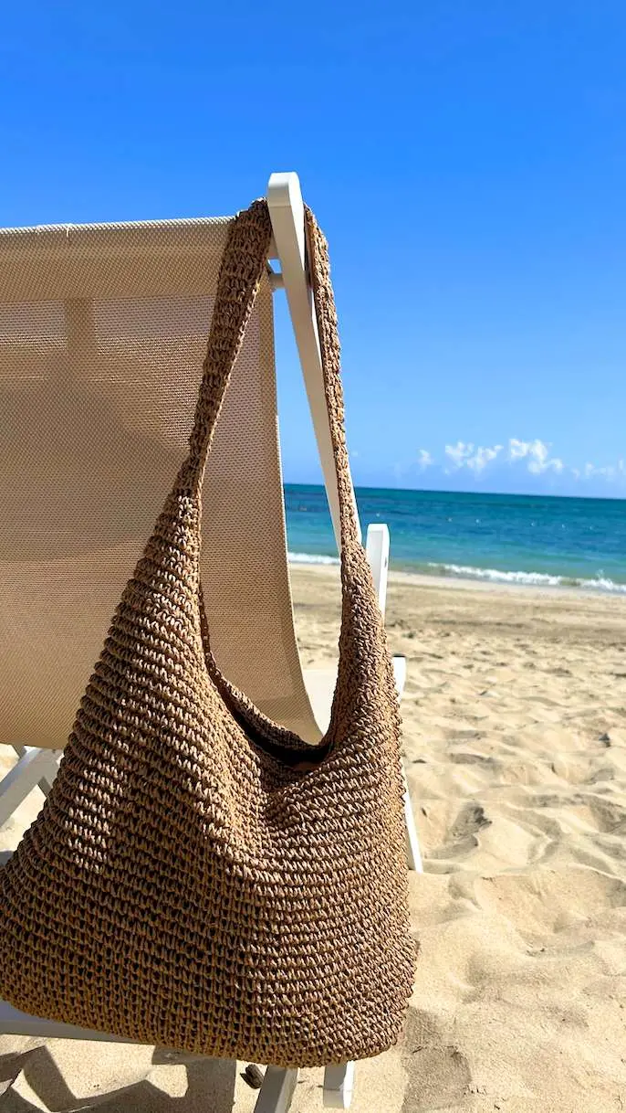 Bolso de playa tejido colgado de una silla frente al mar