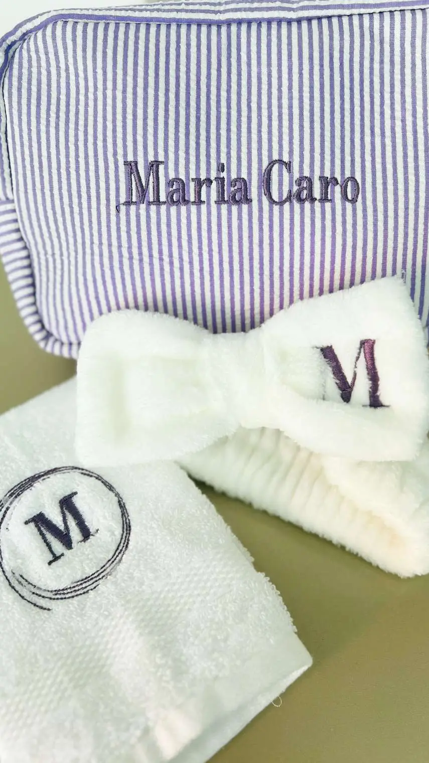 Cosmetiquera lila con un nombre bordado, junto a una balaca y una toalla con la inicial M