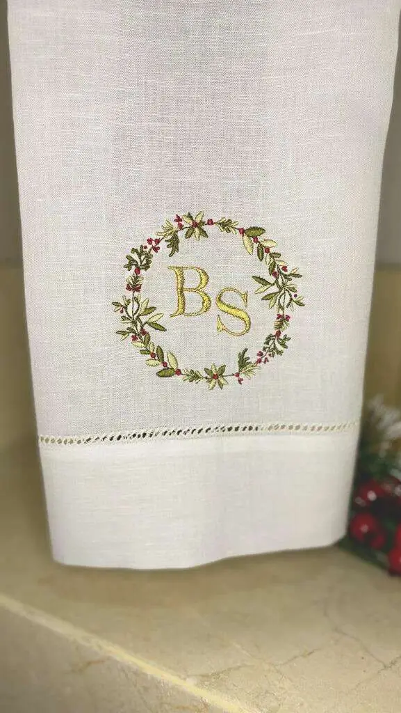 Toalla de cortesía con las iniciales BS dentro de una corona navideña