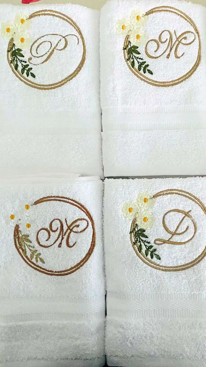 Cuatro toallas de mano con iniciales dentro de coronas de flores bordadas